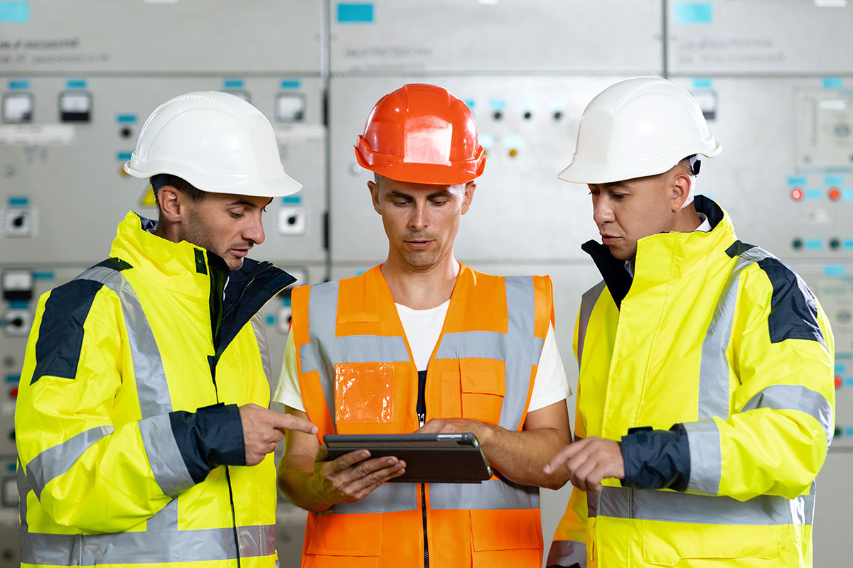 engineers-in-uniform-and-helmets-with-digital-tablet-do-pre-commissioning-works-inspecting-electrical-station-in-sunny-premise